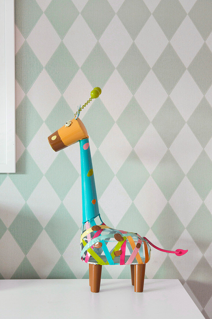 Colorfully painted decorative giraffe against a diamond-patterned wall