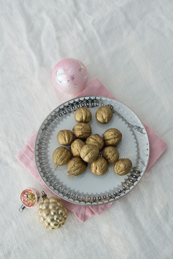 Gold-painted walnuts on ornate plate and Christmas baubles