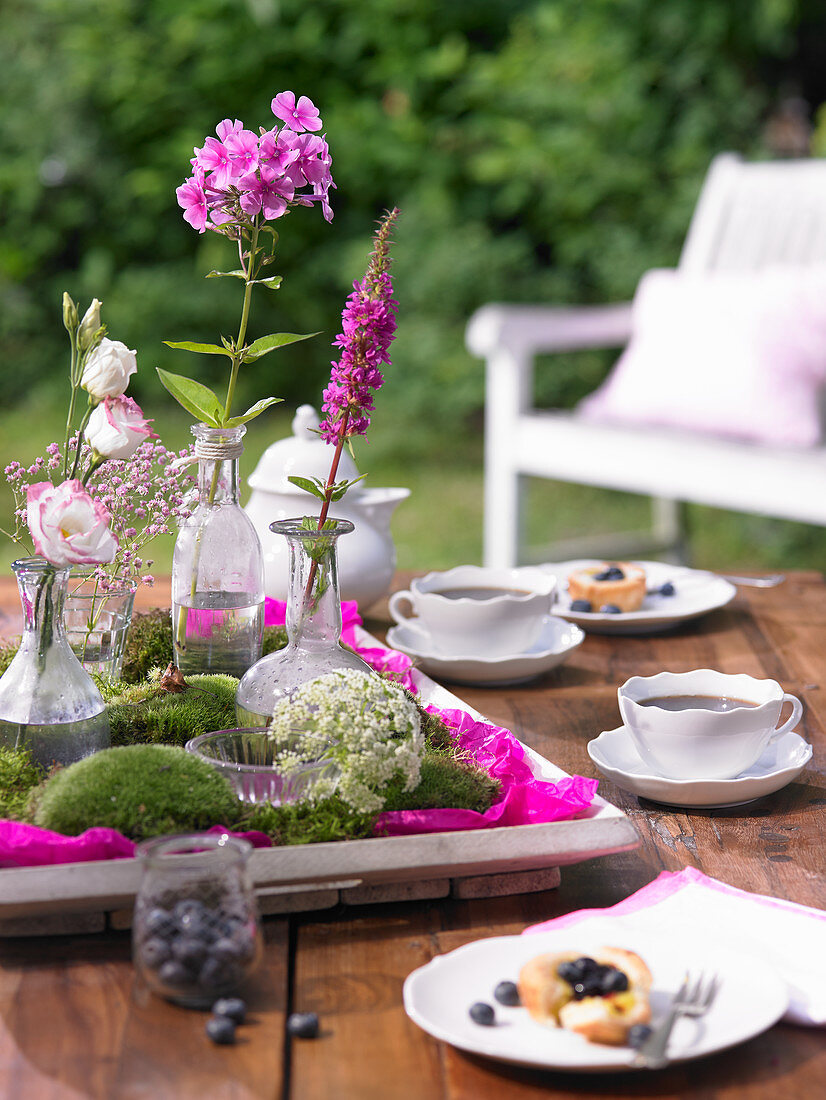 Tablett mit Moos und Blumen auf gedecktem Kaffeetisch im Garten