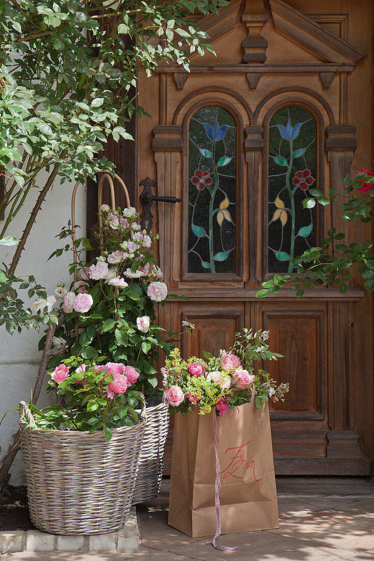 Bouquet of lady's mantle and roses in paper bag and baskets outside front door