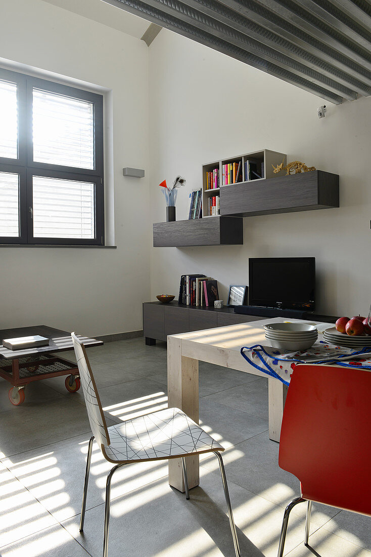 Essbereich mit Designerstühlen, Sideboard mit Fernseher und Wandregal im Industrie-Loft