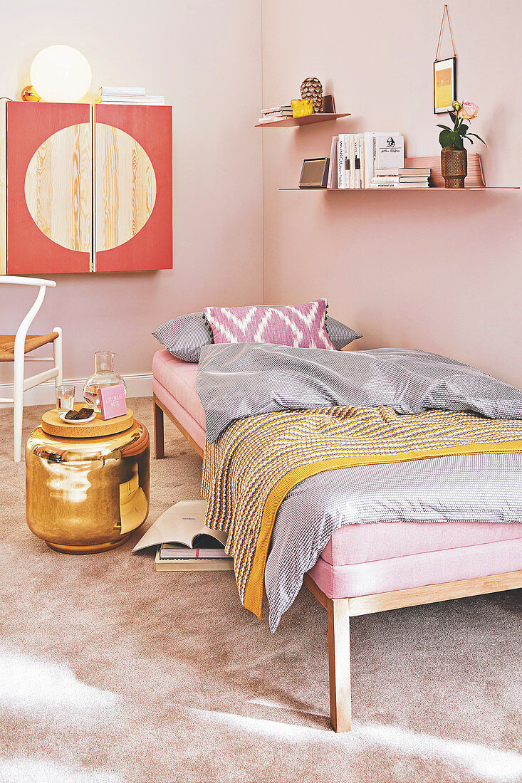 A pink daybed with bedclothes, a golden side table and a wall cupboard