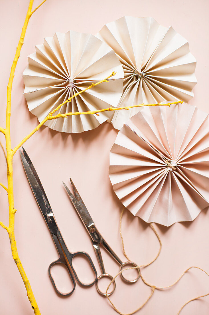 Paper rosettes, scissors and yellow-painted twig on pink surface