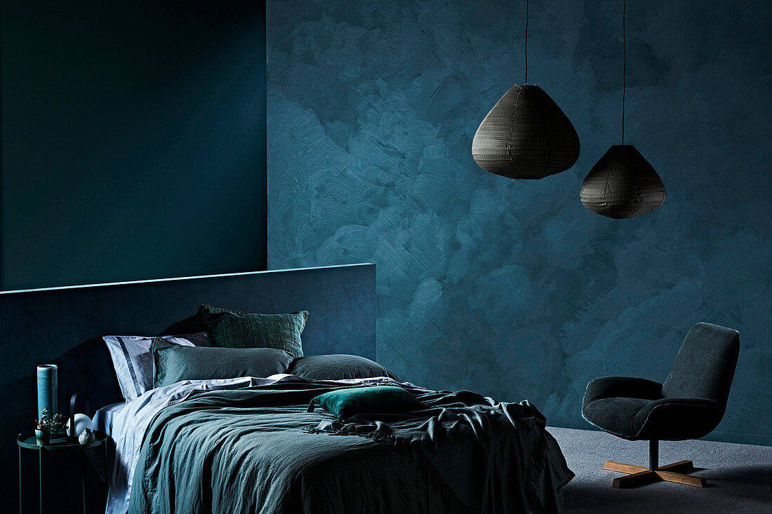 Doppelbett und Sessel im Schlafzimmer mit dunkelblauen Wänden