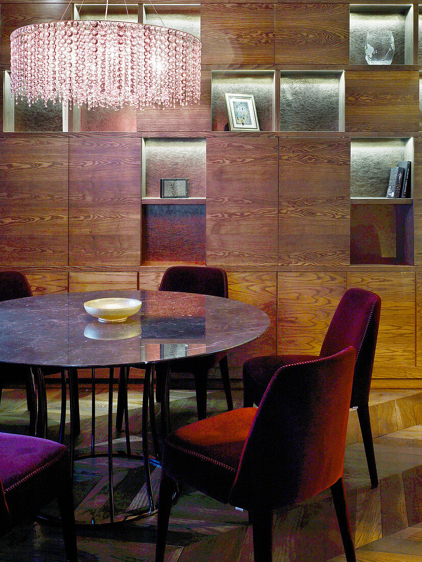Runder Tisch mit gepolsterten Stühlen vor dunkler Regalwand