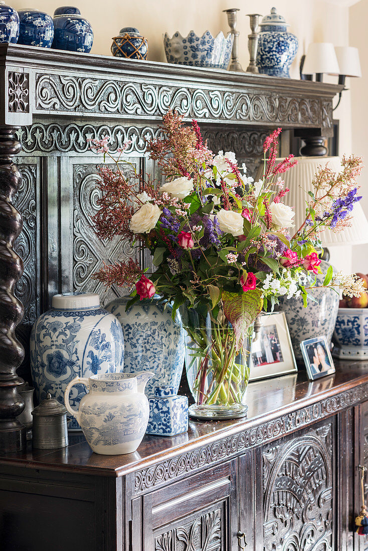 Lavish flower arrangement and vases on antique dresser with ornate carved front