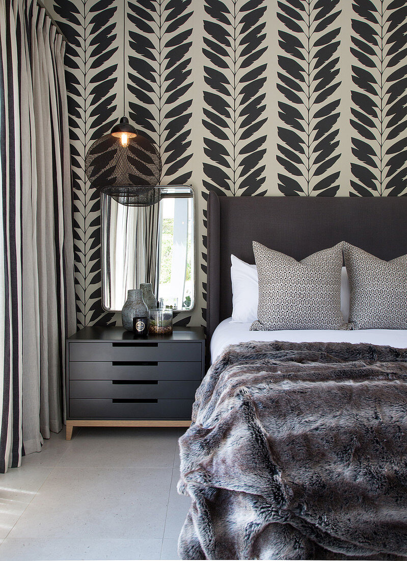 Elegant bedroom in shades of grey with leaf-patterned wallpaper behind bed