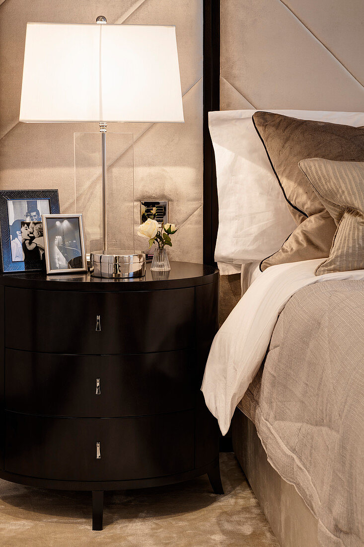 Lamp and photos on stylish bedside cabinet with drawers