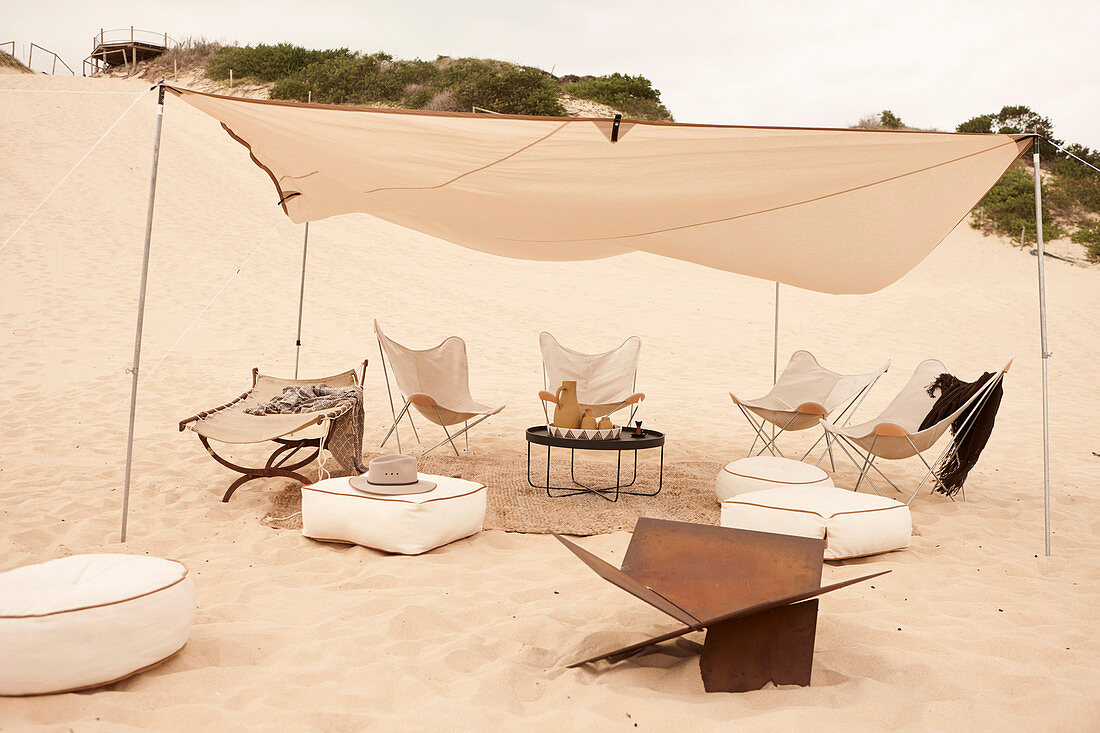 Tisch, Sitzkissen und Butterfly Chairs unter Sonnensegel im Sand