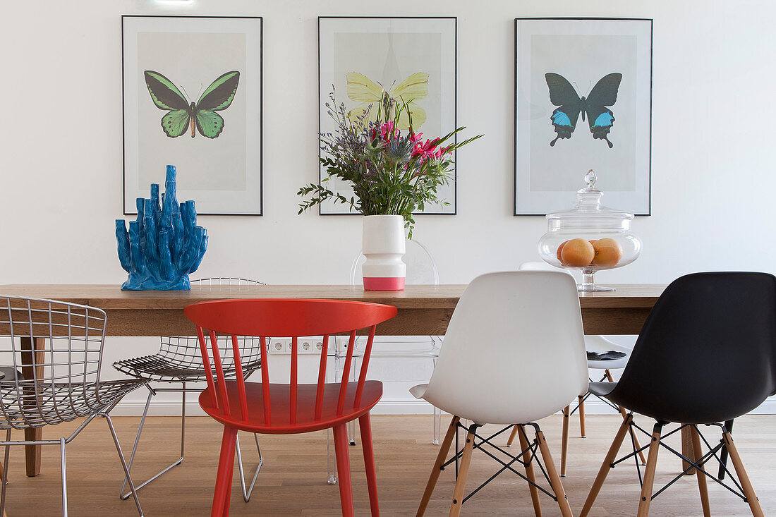 Various designer chairs around dining table in front of pictures of butterflies