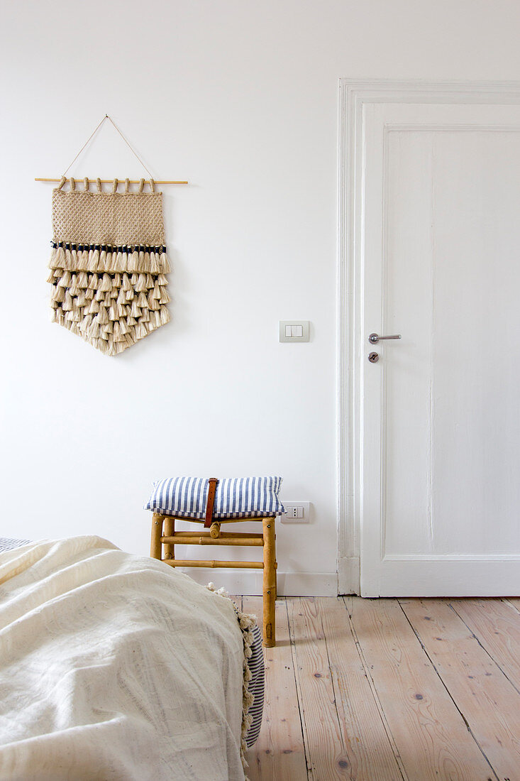Hand-made wall hanging on white wall in bedroom with wooden floorboards