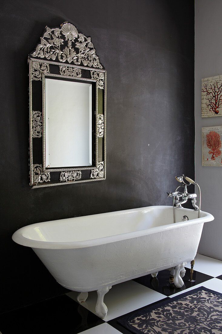 Free-standing bathtub below mirror on dark grey wall