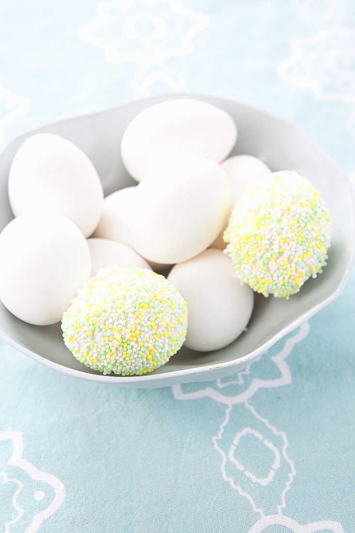 weiße Eier und mit Zuckerperlen verzierte Eier in einer Schale