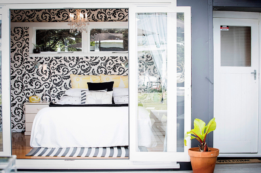 View through open glass sliding door into the bedroom with black and white patterned wallpaper