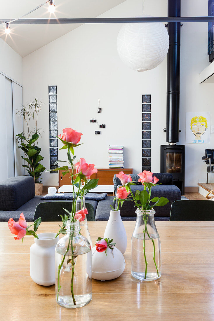 Vasen mit Rosen auf Esstisch, im Hintergrund Loungebereich mit Kaminofen