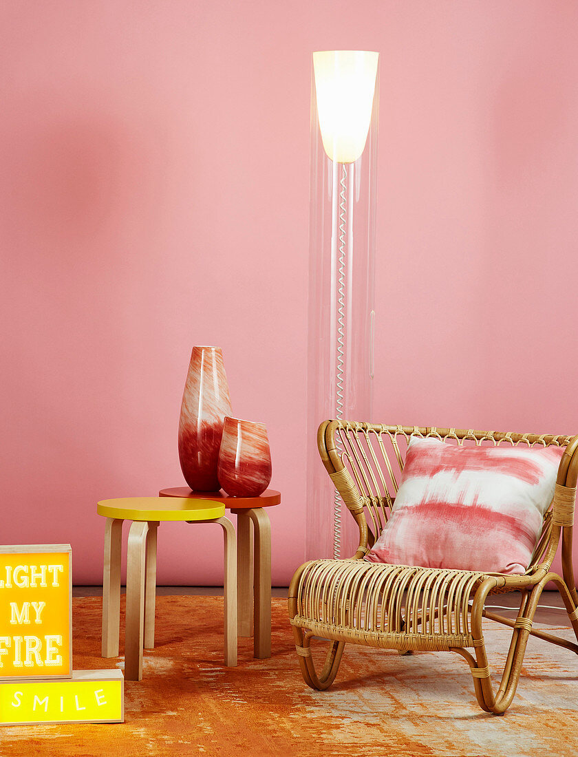 Rattansessel, Designer-Stehlampe und Beistelltische mit Vasen vor rosa Wand