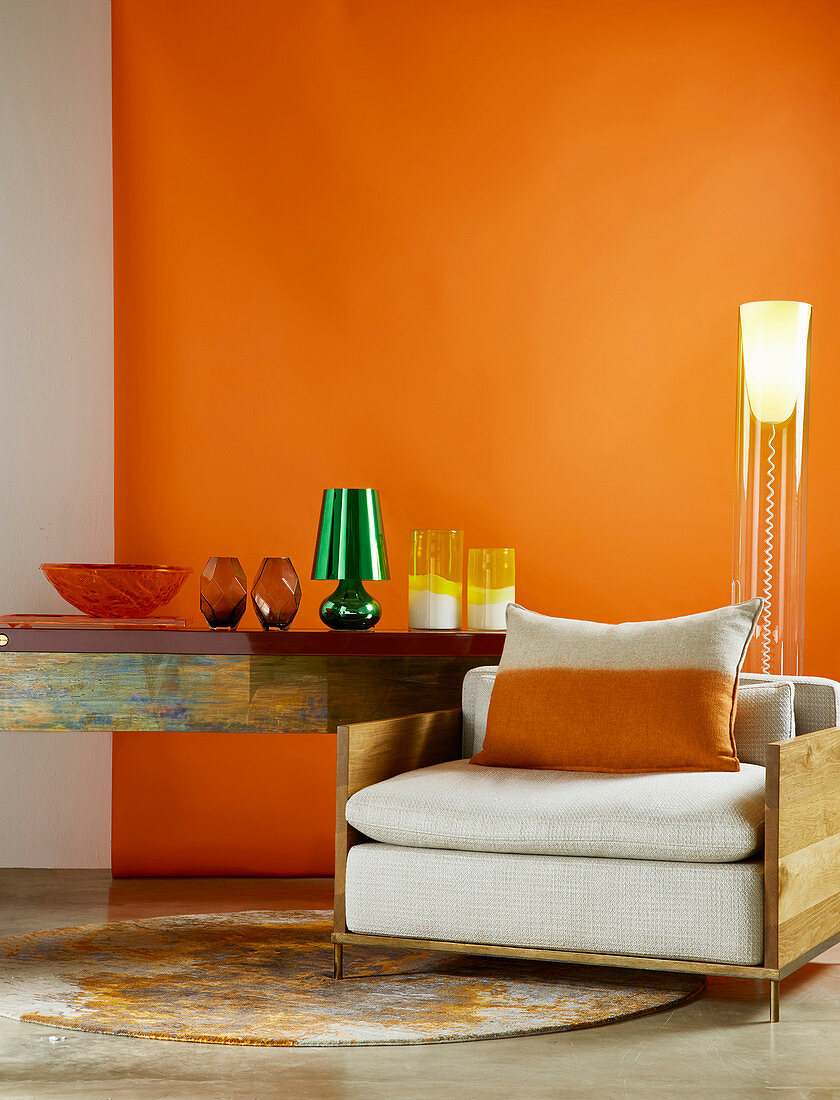 Sessel mit Holzrahmen, Designer-Stehlampe und Konsolentisch mit Glasvasen vor orangefarbener Wand