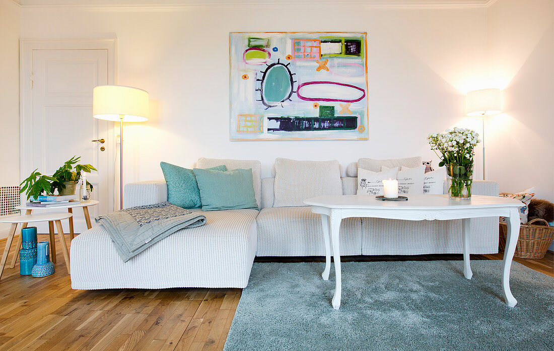 Pale corner sofa, modern artwork, white coffee table, side table and standard lamp in living room