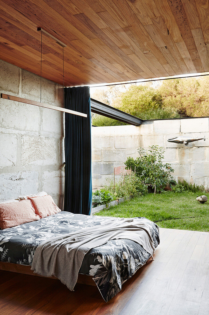 Doppelbett im Schlafzimmer mit Betonwand, Holzdecke und Terrassenzugang