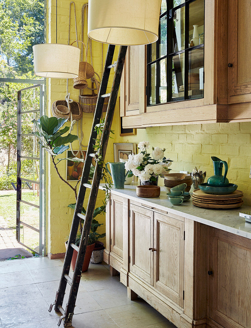 Ladder in front of glass-fronted wall units in country-house kitchen