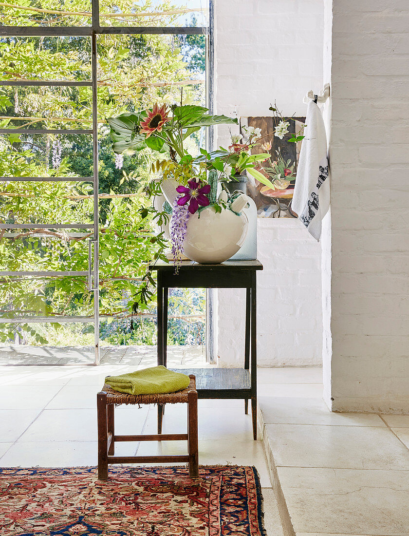 Stool and flowers on side table in bathroom with glass wall overlooking garden