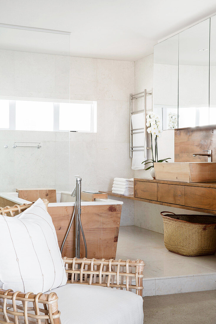 Designerstuhl, Badewanne mit Holzverkleidung und Waschtisch in hellem Badezimmer