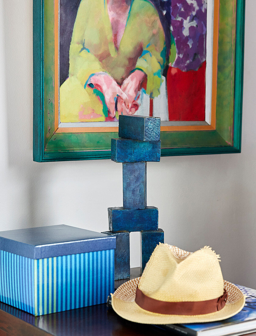 Strohhut, Skulptur und gestreifte Box vor einem Gemälde