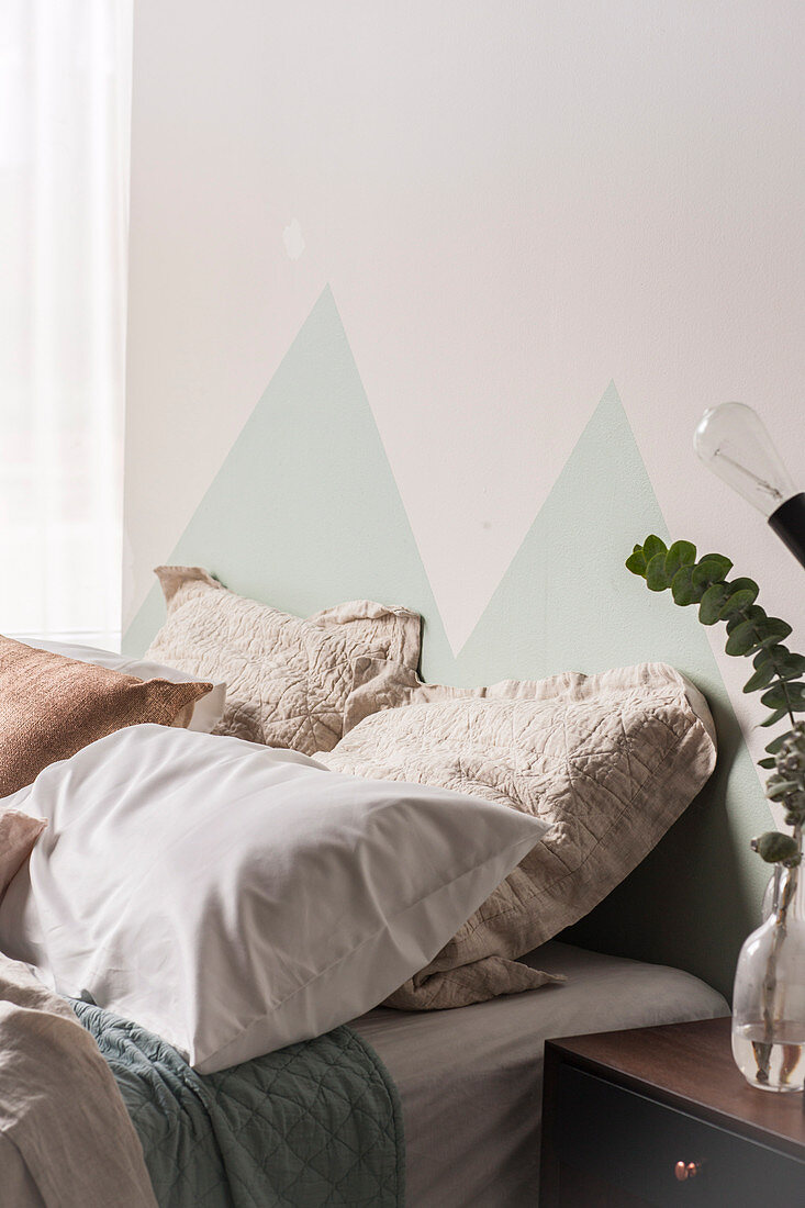Mit Dreiecken bemalte Wand hinter dem Bett mit verschiedenen Kissen