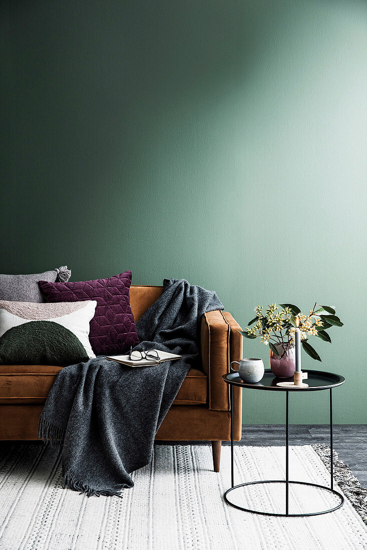 Braunes Sofa mit Kissen und Plaid vor einer leeren grünen Wand