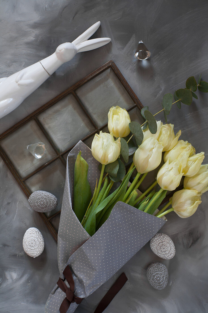 Ein Bund weiße Tulpen im grauen Papier mit Osterdeko