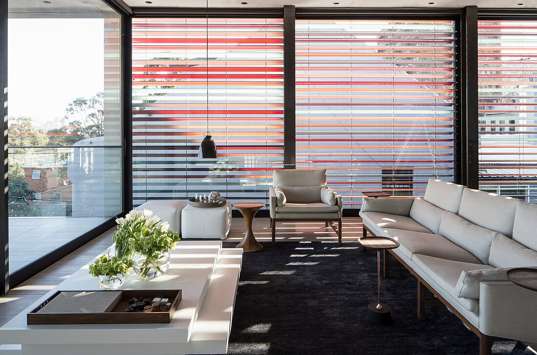 Weisses Designer-Sofa vor Rundum-Fensterfront mit Aluminium-Jalousie