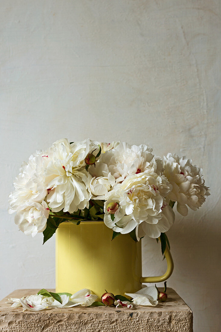 Bouquet of white peonies in yellow enamel jug on stone slab