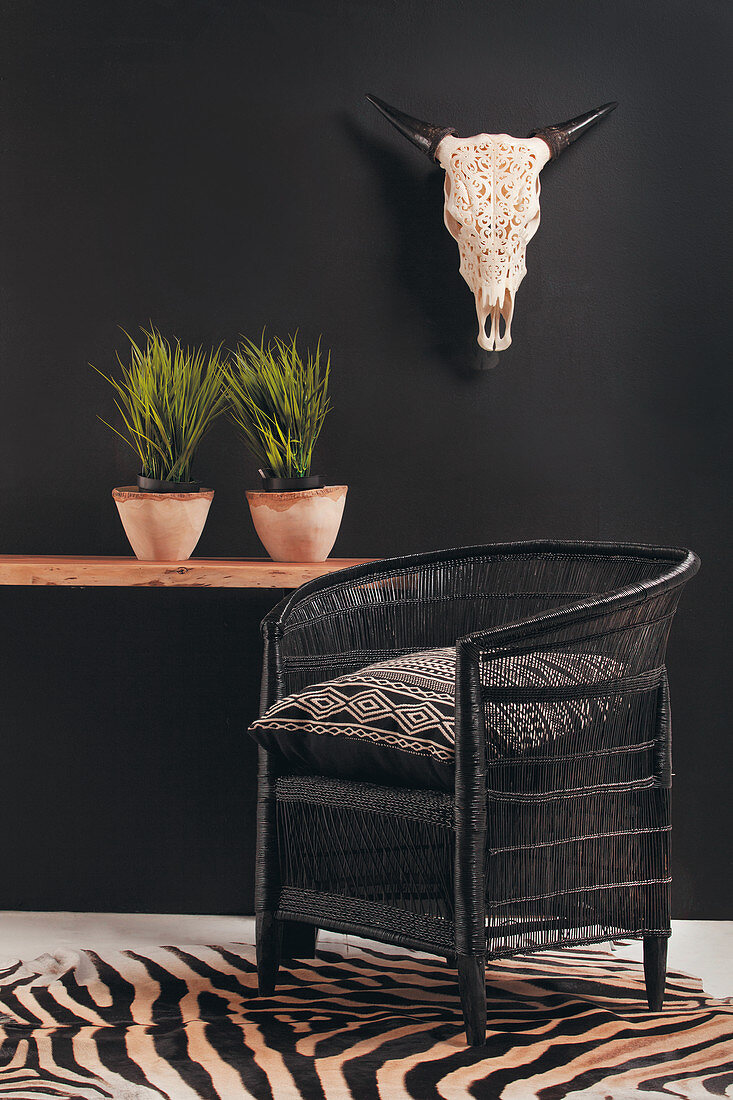 Black wicker armchair on zebra-patterned rug against black wall