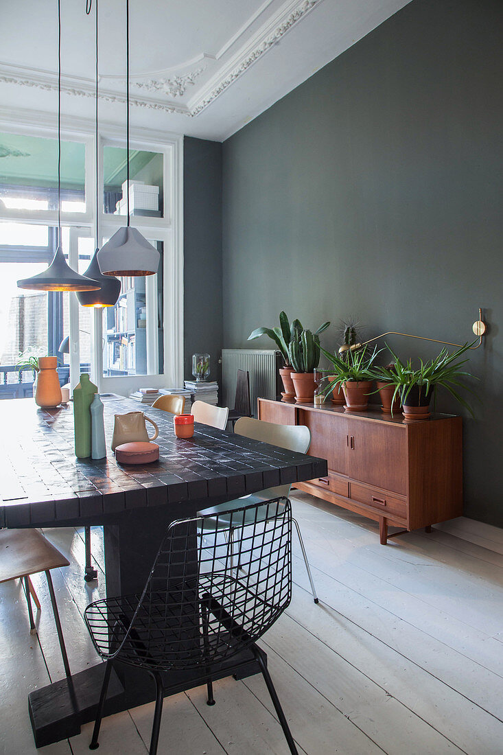 Langer Esstisch mit Klassikerstühlen und Sideboard mit Topfpflanzen im Esszimmmer mit dunkler Wand und weißer Dielenboden