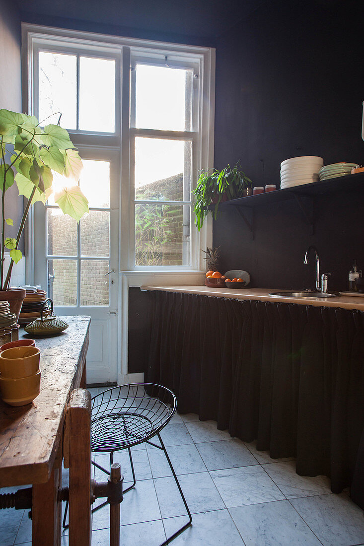 Küchenzeile mit Vorhang und alter Tisch mit Geschirr in Küche mit dunkler Wand