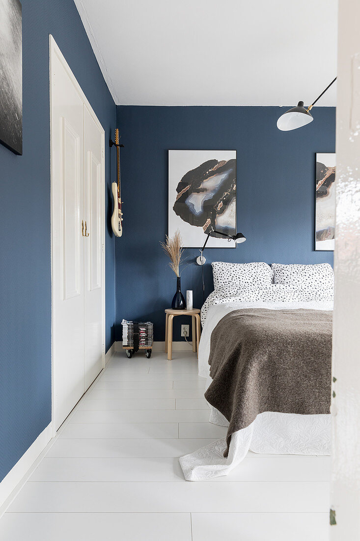 Doppelbett im Schlafzimmer mit blauer Tapete, großformatigen Kunstwerken und weißer Dielenboden