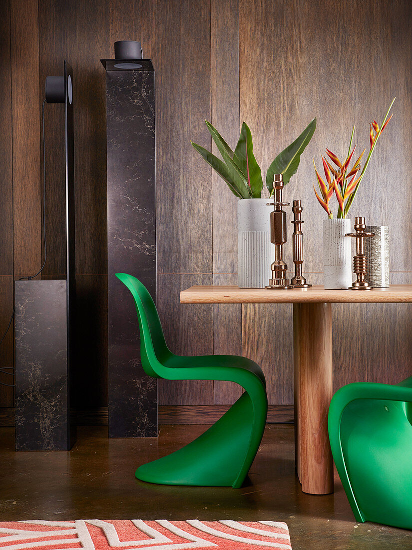 Designer-Stehleuchte, Holztisch mit Vasen und Kerzenhaltern und grüner Panton-Stuhl vor Wand mit dunkler Holzverkleidung