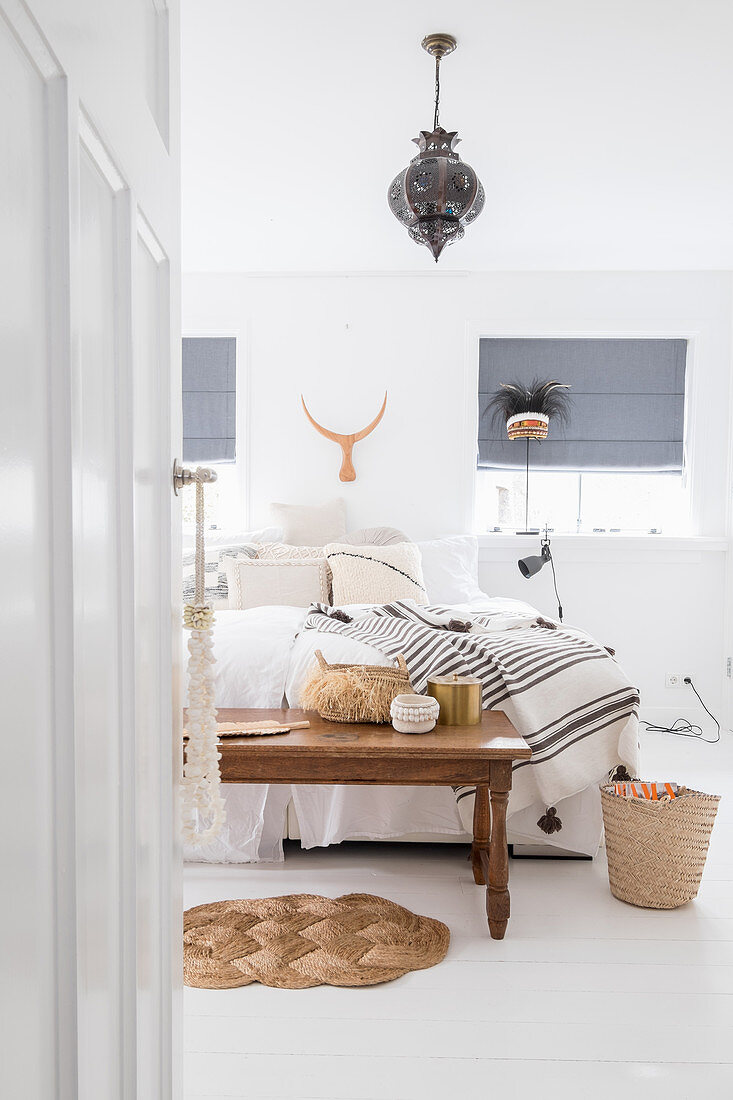 Blick auf Holztisch und Doppelbett in weißem Schlafzimmer