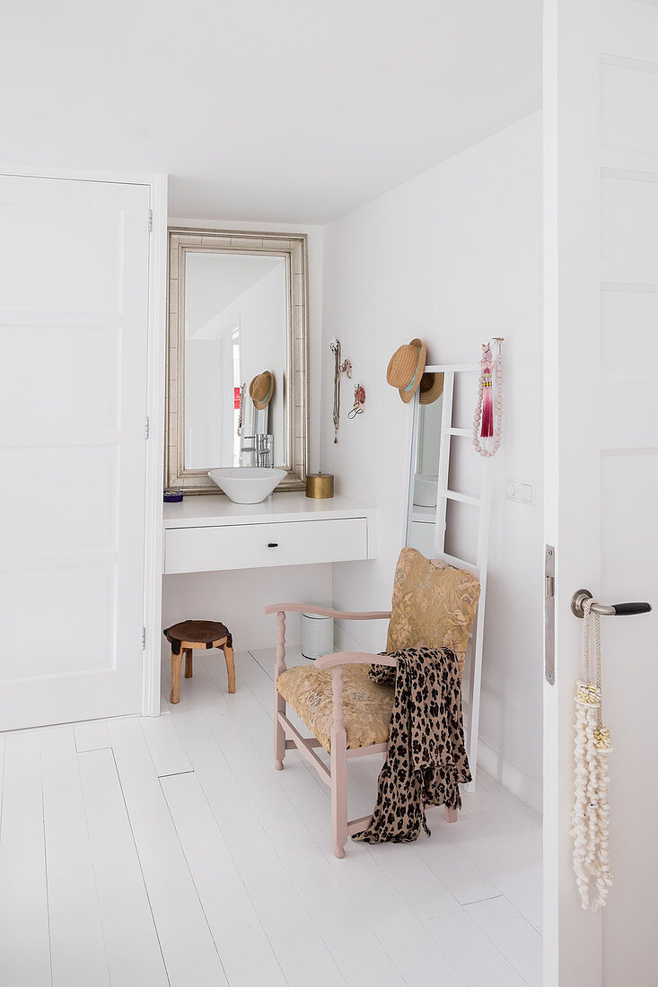 Antique chair, mirror and ladder in front of small washstand in white bathroom