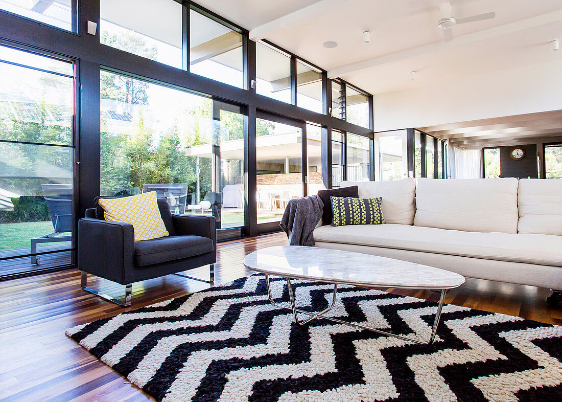 Teppich mit schwarz-weißem Zig-Zag-Muster, Coffeetable, Couch und Sessel vor Glasfront in offenem Wohnraum