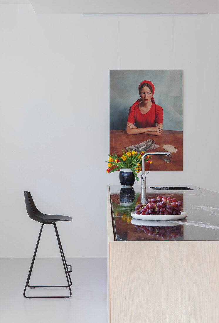 Black bar stool at kitchen island below portrait of woman on wall