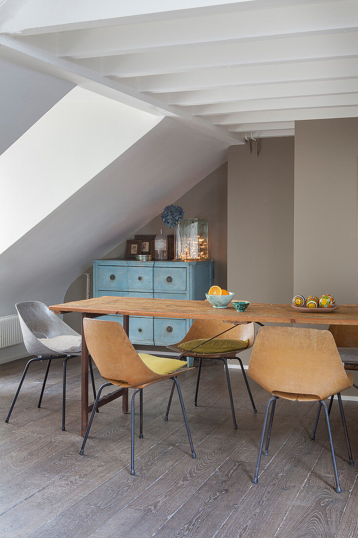 Shell chairs around narrow wooden table in attic interior