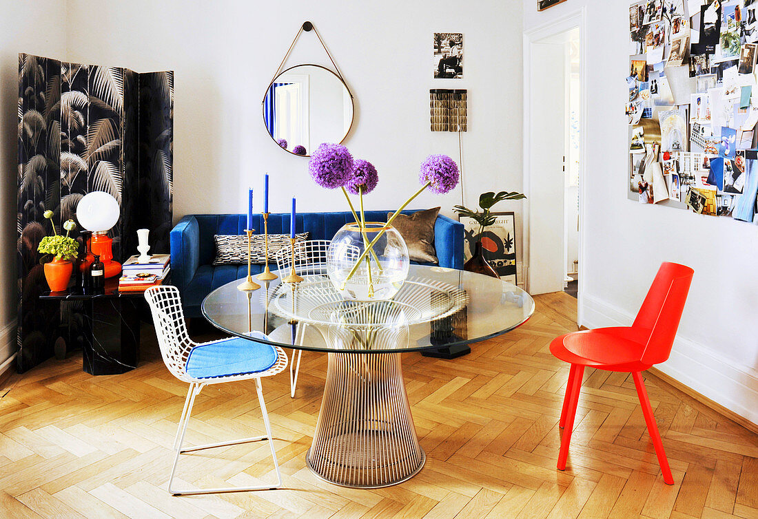 Metalltisch mit runder Glasplatte, verschiedene Stühle, Paravent und blaue Couch im Wohnzimmer