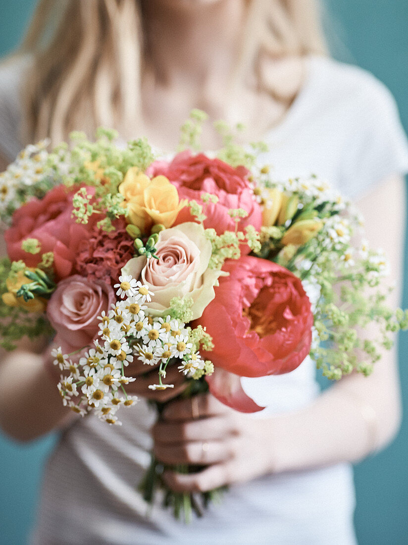 Frau hält Blumenstrauss aus Rosen, Pfingstrosen, Fresien und Kamillenblüten