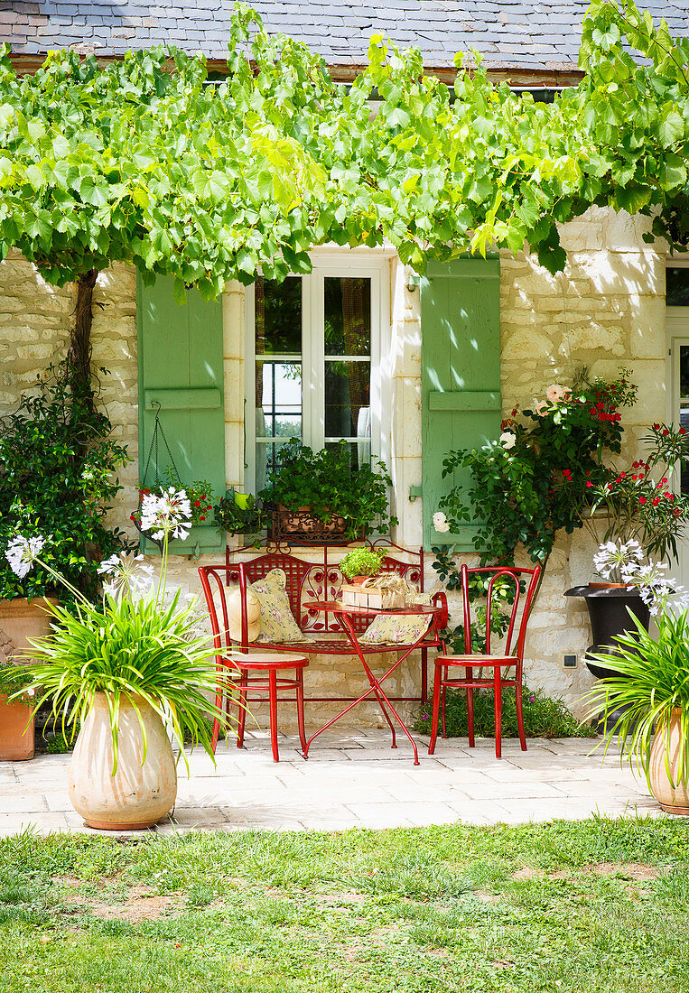 Sitzplatz mit roten Gartenmöbeln vor französischem Steinhaus