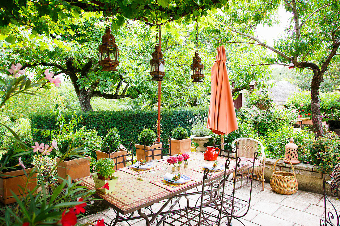 Mosaic table and metal chairs on terrace in lush garden
