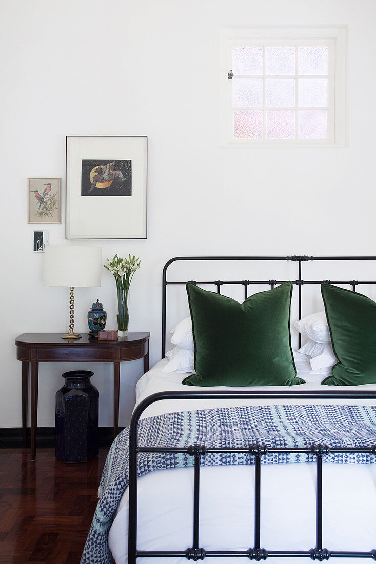 Doppelbett mit Metallgestell, grüne Kopfkissen und Konsolentisch als Nachttisch