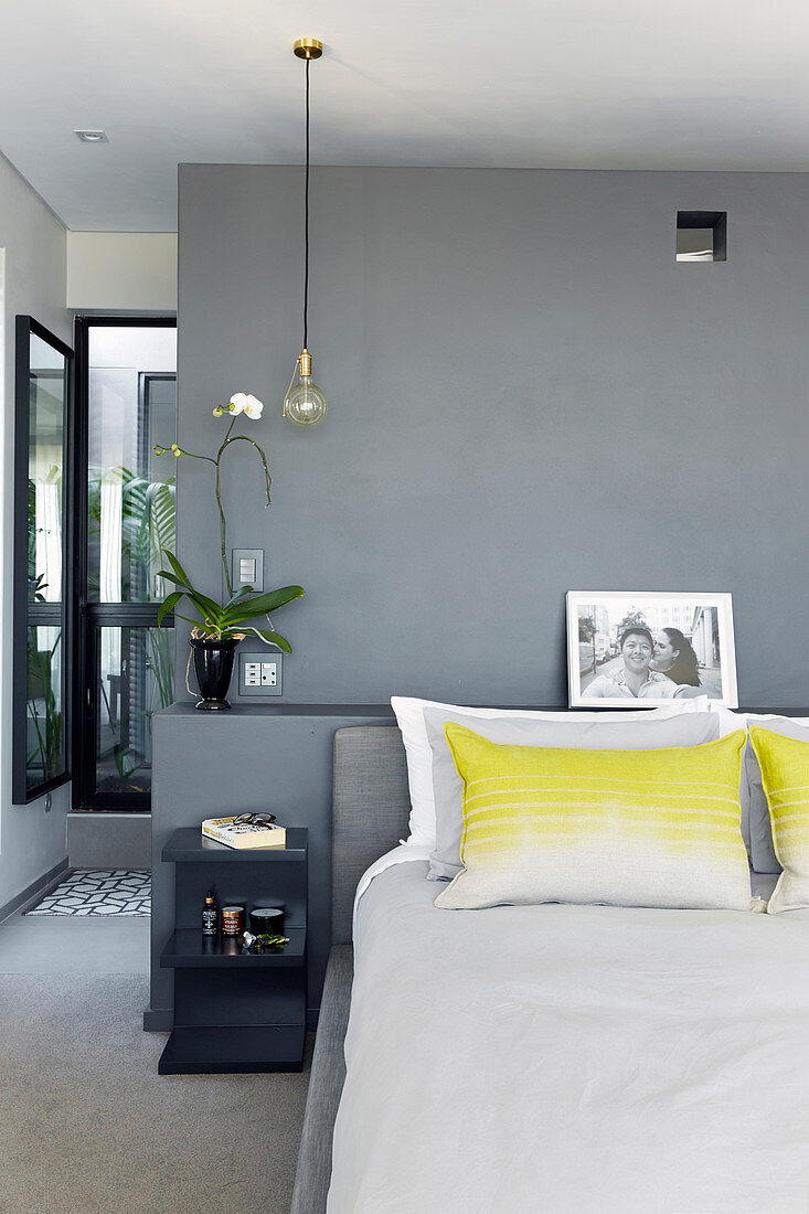 Pillows with splash of yellow on double bed in bedroom with grey-painted wall