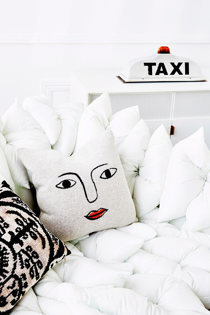 White pillow sofa with decorative pillows, in the background a taxi light as a table lamp