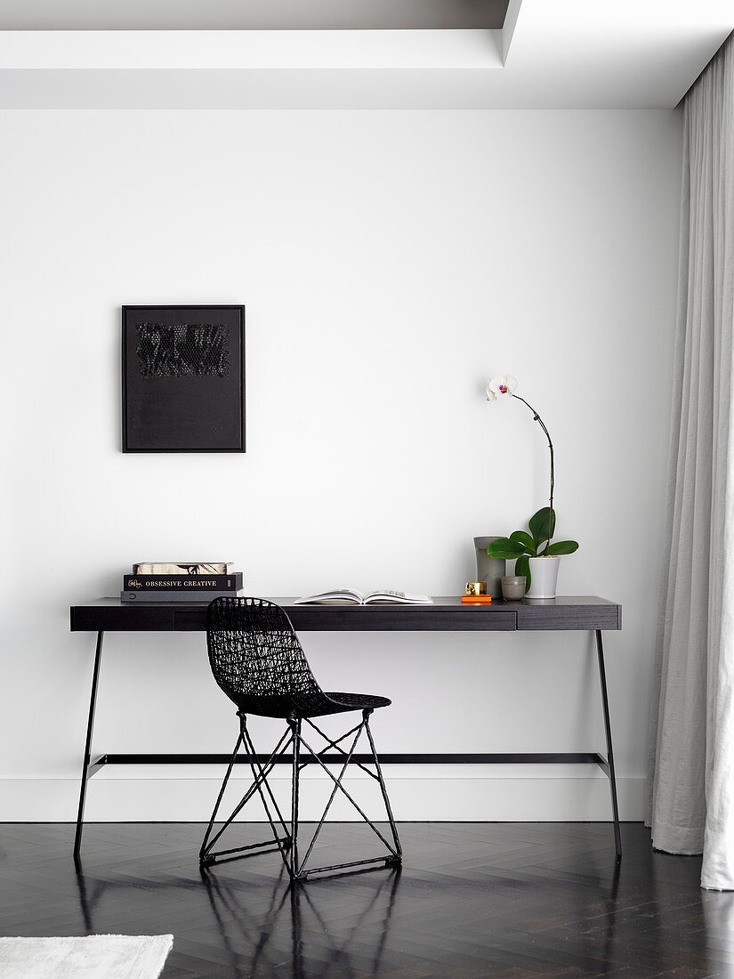 Kleiner Arbeitsplatz mit schwarzem Tisch und Designerstuhl an weißer Wand